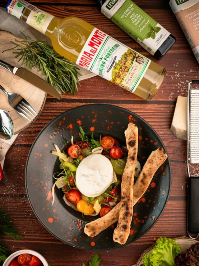 A colorful Mediterranean diet plate with fresh vegetables, olives, grilled fish, whole grains, and olive oil on a rustic wooden table.