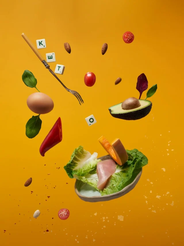“Top view of keto-friendly foods including avocado, eggs, salmon, leafy greens, nuts, and olive oil arranged on a wooden table — ideal for a low-carb diet.